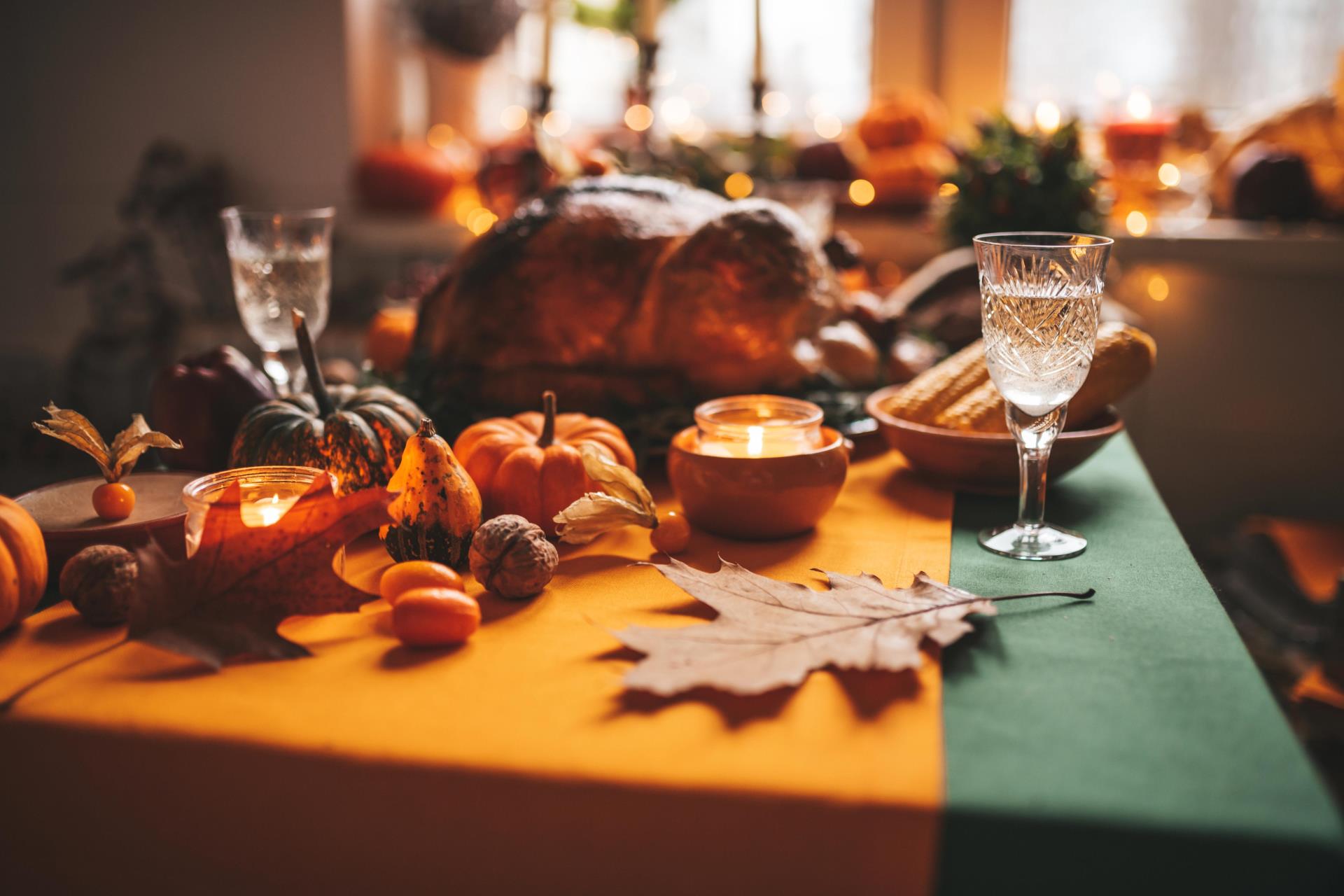 Thanksgiving day dinner with holiday autumn decor and candles. Family dining room table set with delicious golden roasted turkey on platter garnished rosemary and fresh small pumpkins