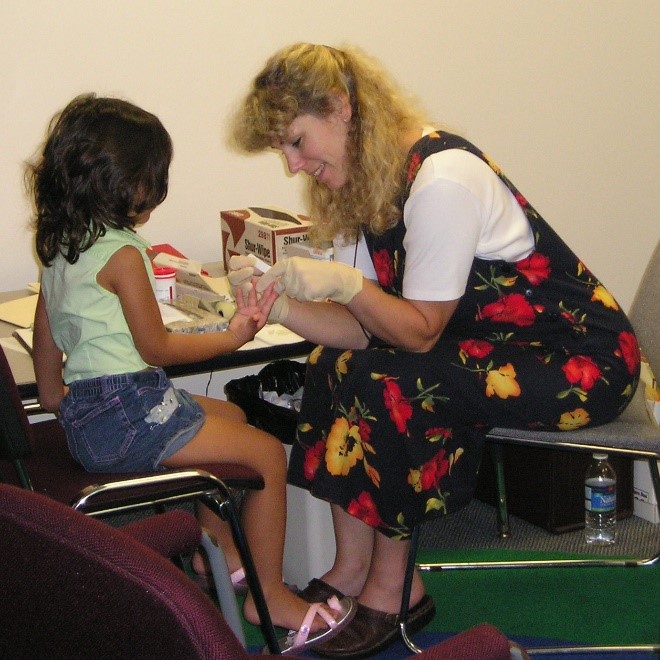 Picture of a nurse getting a lead blood sample from a child by pricking her finger